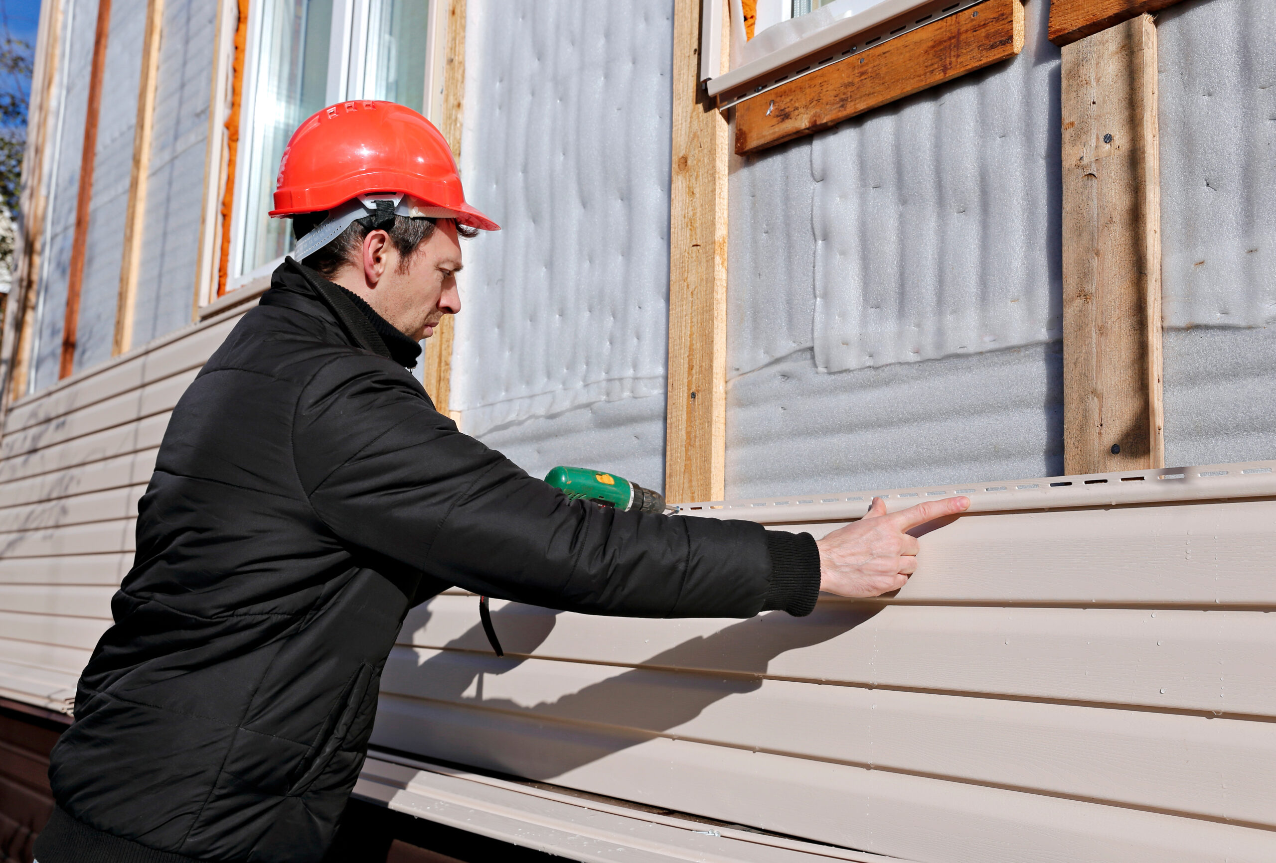 Handsome young man builder installing exterior wood siding
